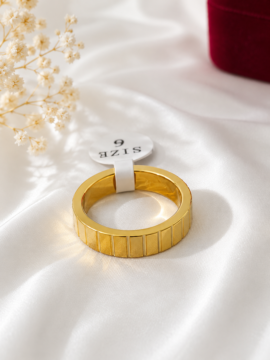 Minimalist gold textured band ring displayed on soft white fabric with floral accents.