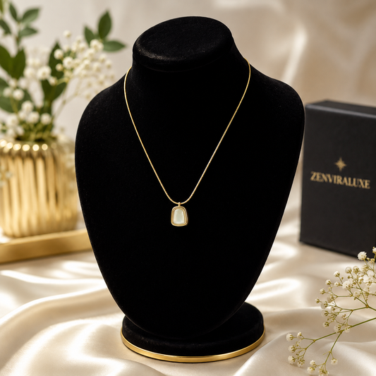 Elegant gold-tone necklace with a pearl-inspired pendant displayed on a black velvet jewelry stand with luxury floral decor and ZenviraLuxe packaging.