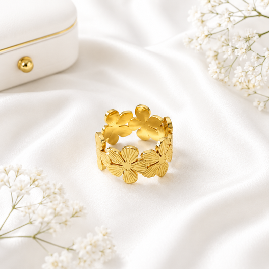 Gold floral statement ring with detailed flower petals displayed on soft white fabric beside a luxury jewelry box and delicate white flowers.