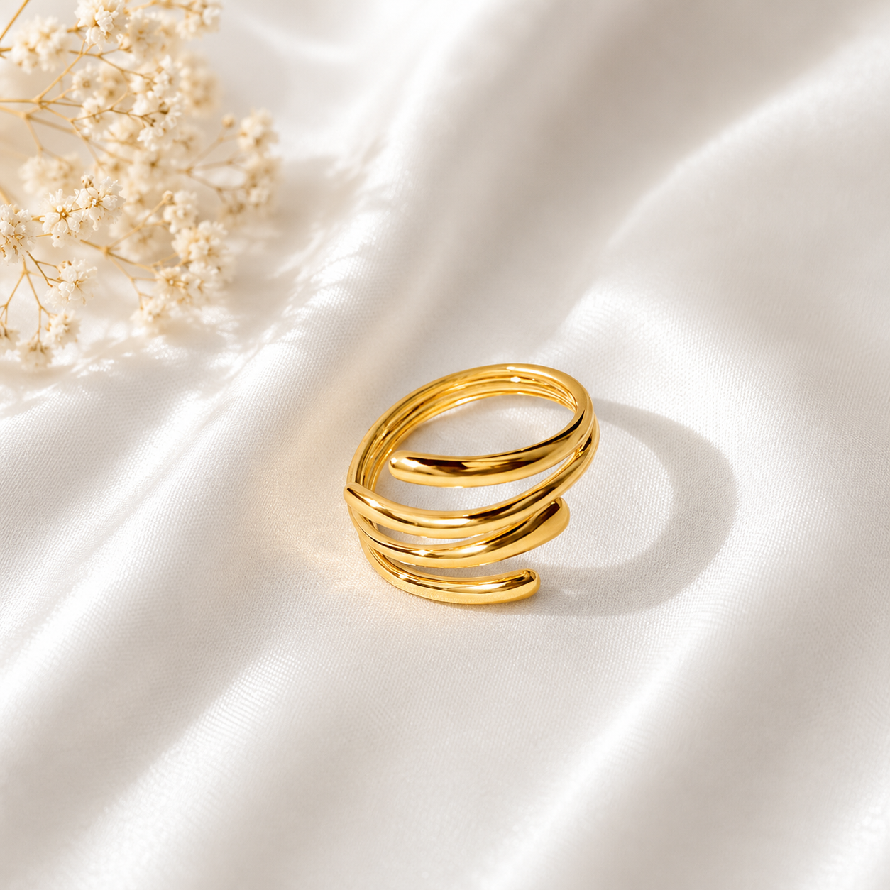 Elegant gold spiral ring with layered wrap design displayed on soft white fabric background.