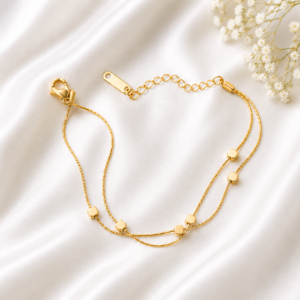 Minimalist double-layer gold bracelet with polished square accents displayed on a white satin background