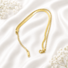 Luxury dual-chain gold bracelet with snake chain and bead chain displayed on a white satin background