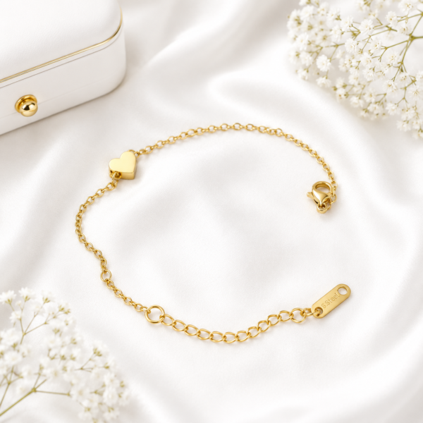 Minimal gold stainless steel bracelet with polished heart charm displayed on a white satin background