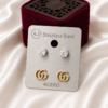 Crystal stud earrings and gold Double G logo ear studs on a stainless steel display card.