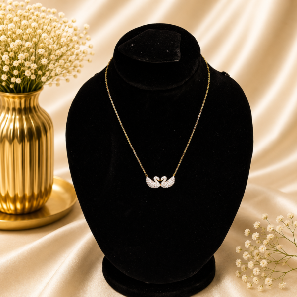 Gold stainless steel necklace with a crystal twin swan heart pendant displayed on a black velvet jewelry bust.