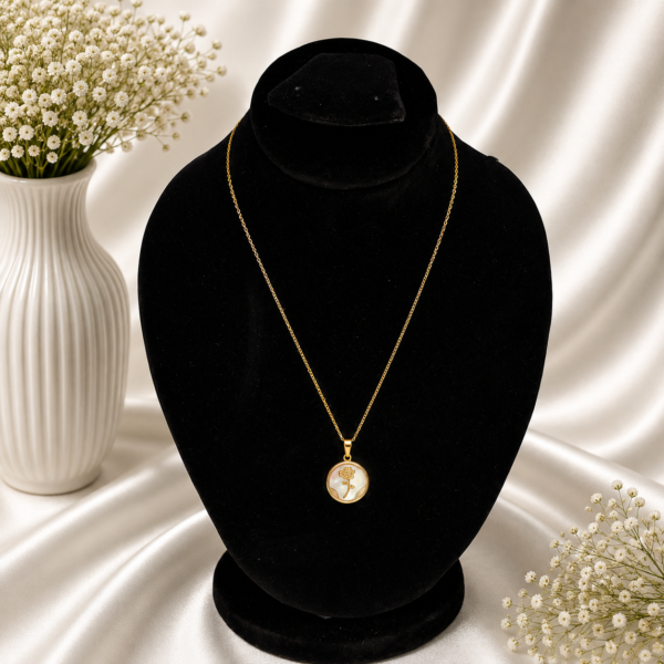 Gold stainless steel necklace featuring a round pearl-inspired pendant with a delicate rose design displayed on a black velvet jewelry bust.