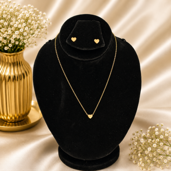 Gold stainless steel heart pendant necklace with matching heart stud earrings displayed on a black velvet jewelry bust.