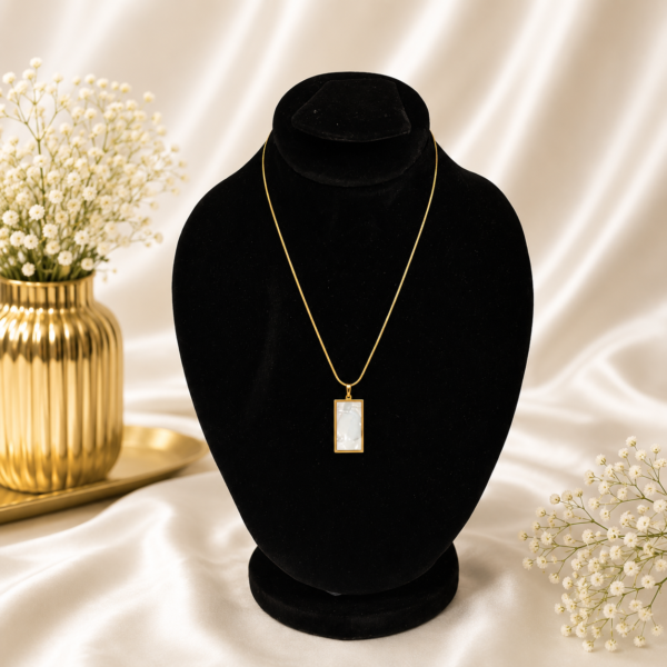 Gold stainless steel necklace with a white marble-style rectangle pendant displayed on a black velvet jewelry stand.