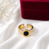 Gold stainless steel Roman numeral ring with crystal accents and a black centerpiece displayed on a white satin background.