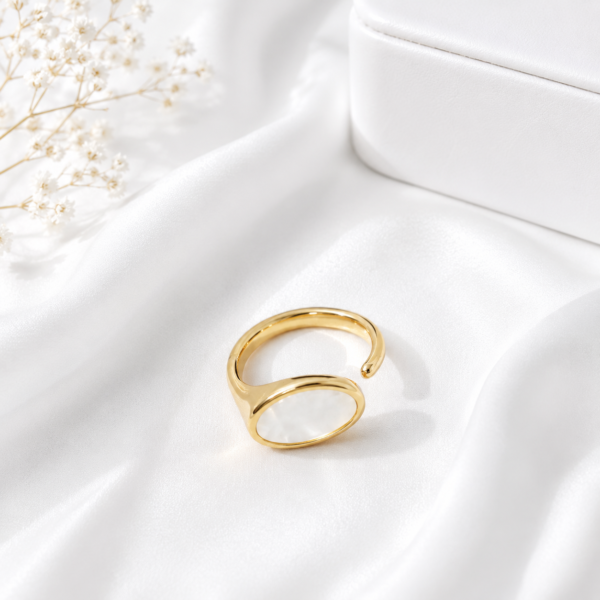 Adjustable gold stainless steel ring with an oval pearl-inspired centerpiece on a white satin background.