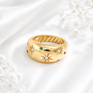 Gold stainless steel ring with crystal star engravings and colorful accent stones on a white satin background.