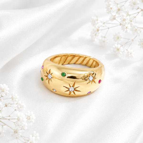 Gold stainless steel ring with crystal star engravings and colorful accent stones on a white satin background.
