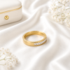 Gold stainless steel band ring with crystal accents displayed on a white satin background.